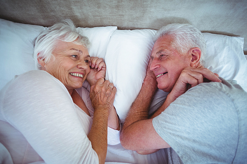 Overhead view of happy senior couple looking at each other while lying on bed