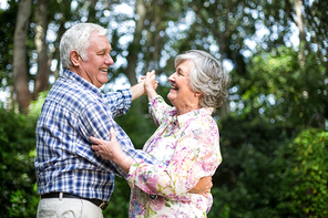 Cheerful senior couple dancing against trees in back yard