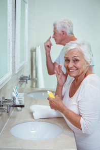 Senior woman applying cream with husband while standing in bathroom