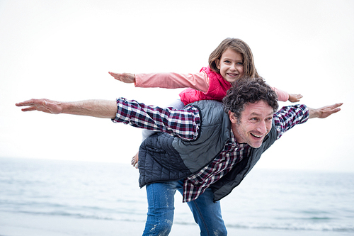 Close-up of happy father carrying daughter on back at sea shore