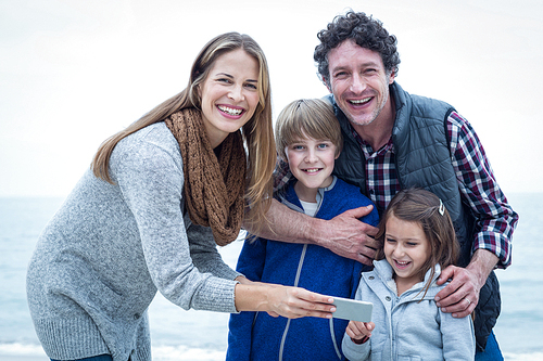 Portrait of cheerful family with mobile phone enjoying at beach