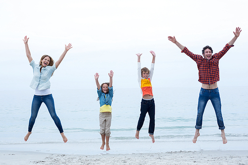 Full length of family jumping with arms raised at sea shore