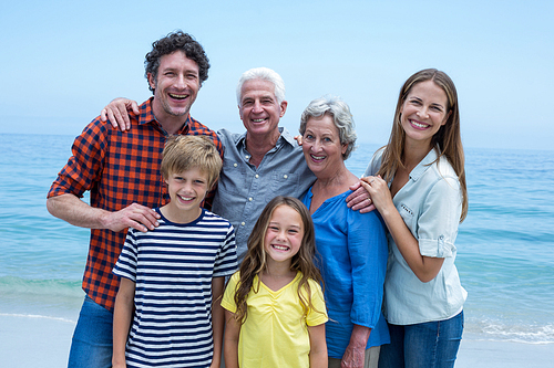 Portrait of cheerful multi-generation family standing at sea shore against blue sky