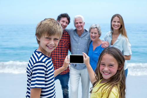 Portrait of happy siblings photographing family with smartphone at sea shore