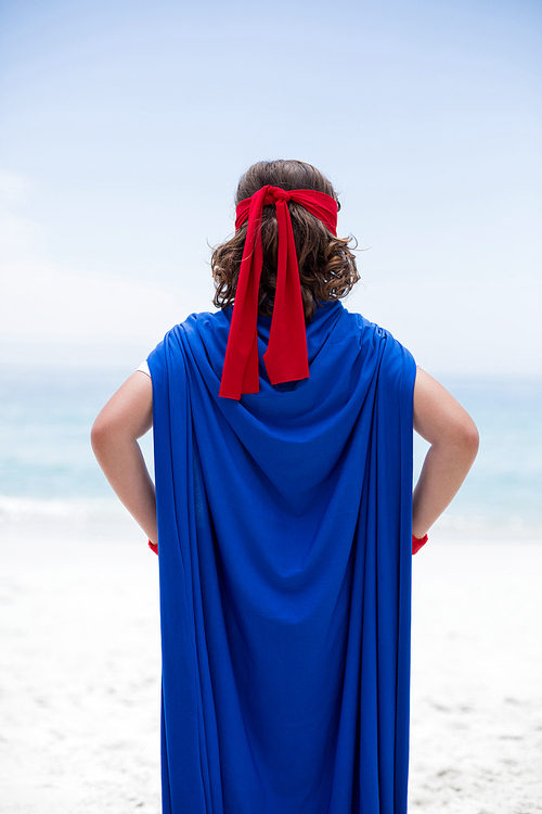 Rear view of boy in superhero costume standing at sea shore against sky