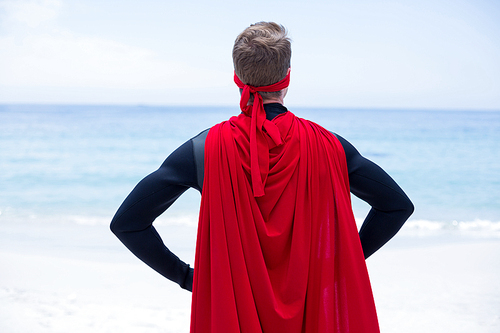 Rear view of superhero costume with hand on hip at sea shore against sky