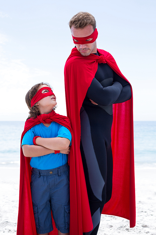 Father and son in superhero costume standing with arms crossed at beach