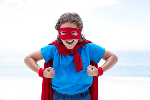 Portrait of cheerful boy in superhero costume flexing muscles at sea shore