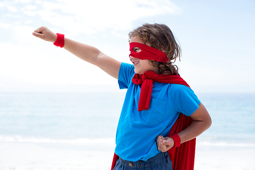 Cheerful boy in superhero costume pretending to fly at sea shore