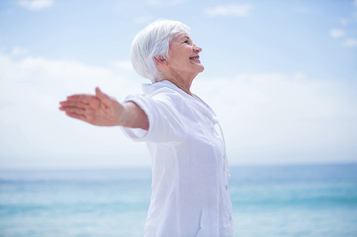 Side view of senior woman smiling while exercising at beach against sky