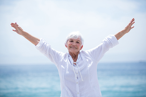 Portrait of happy senior woman standing with arms outstretched at sea shore