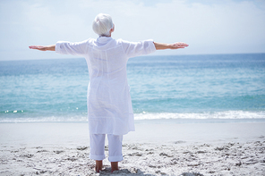 Rear view of senior woman exercising at sea shore on sunny day