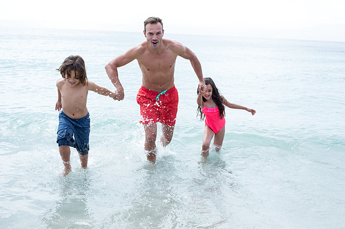 Happy father running with children at beach against sky