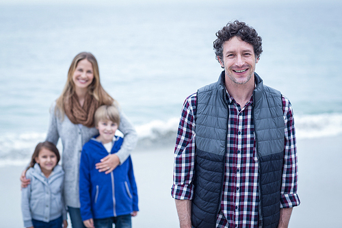 Portrait of happy father with children and mother in background at beach