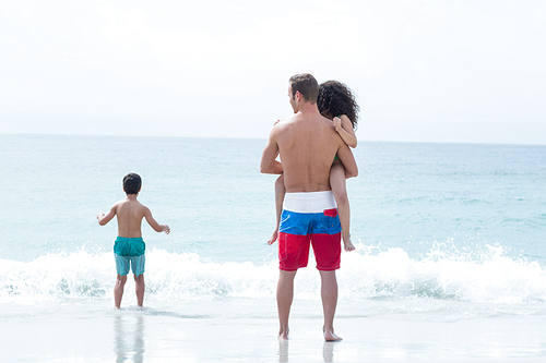 Father carrying daughter while son standing on sea shore at beach