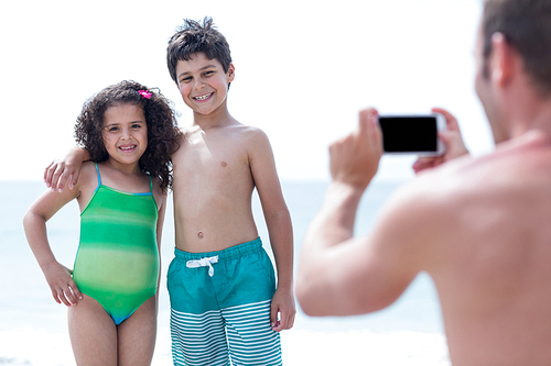 Father photographing smiling children while standing at beach