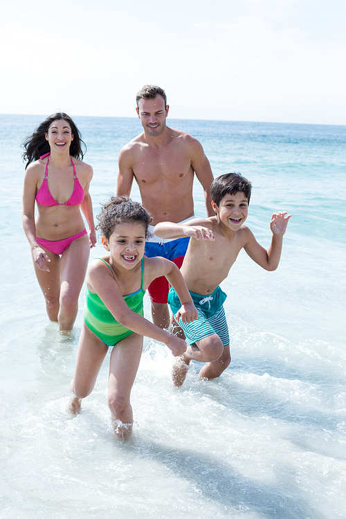 Parents walking while children running on sea shore at beach