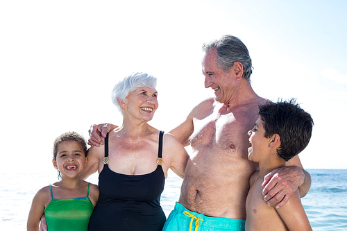 Happy granparents with grandchildren standing against sky at beach