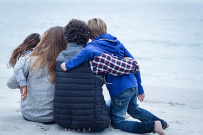 Rear view of family sitting on sea shore at beach