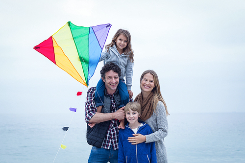 Portrait of cheerful family with kite at sea shore