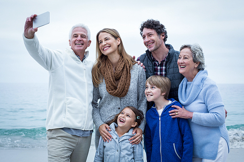 Grandfather taking selfie with cheerful family at sea shore against sky