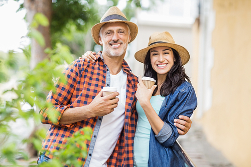 Portrait of happy couple with coffee cups standing in city