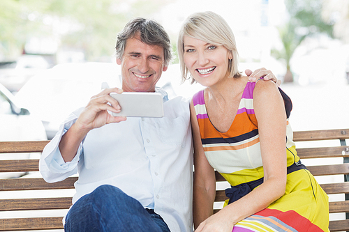 Happy couple with smartphone sitting on bench in park