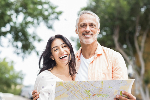 Portrait of happy couple holding map in city