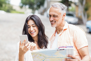 Smiling couple using phone while holding map in city