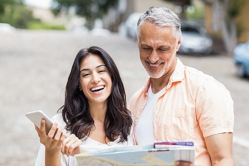 Portrait of happy beautiful woman holding phone while man reading map in city