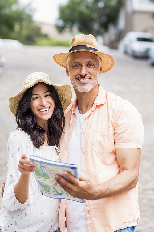 Portrait of smiling couple holding map while standing on street in city