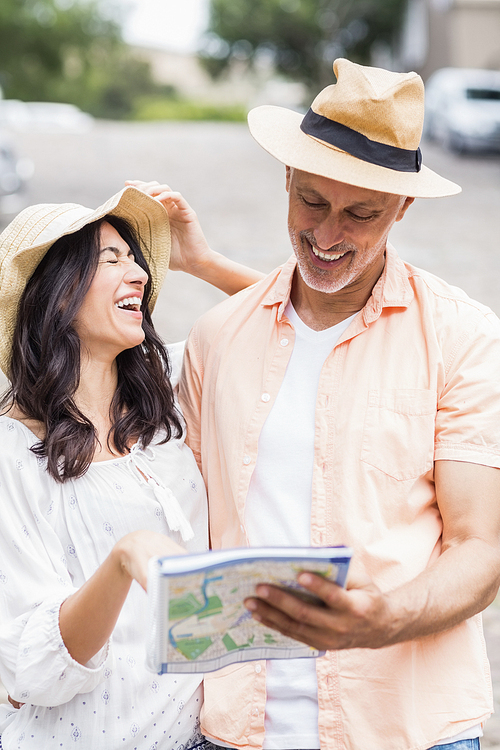 Happy couple reading map while standing on street in city