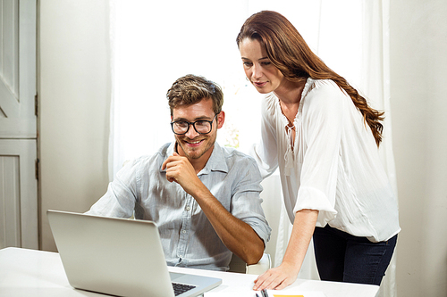 Male and female collegues using laptop at desk in office