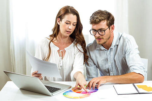 Male and female collegues discussing colour samples at desk in creative office