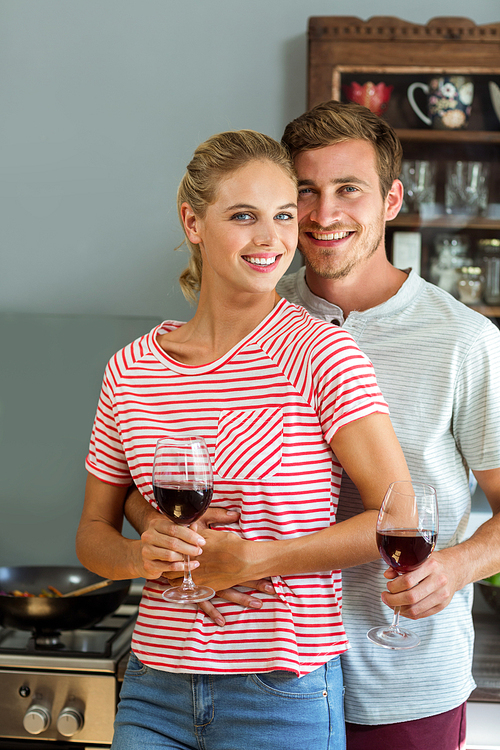 Portrait of smiling young couple holding wineglasses in kitchen at home