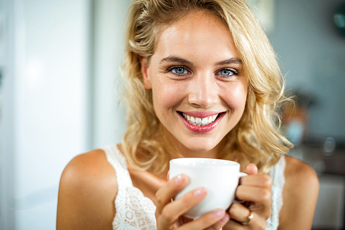 Close-up portrait of smiling beautiful woman holding coffee cup at home