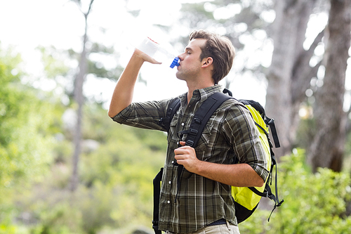 Side view of young man drinking water while standing in forest