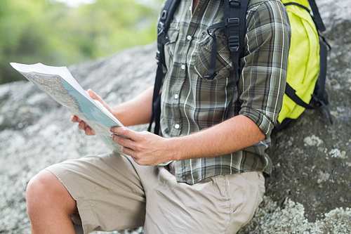 MId section of hiker holding map while leaning on rock
