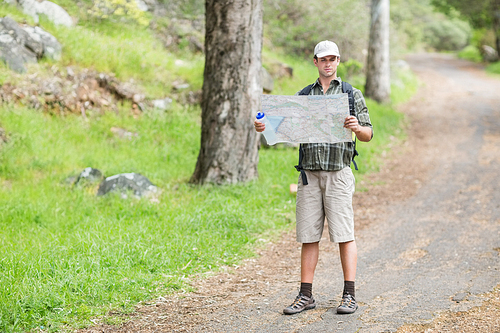 Young man reading map while standing on footpath in forest