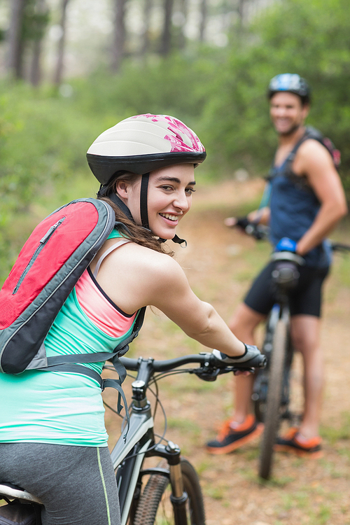 Portrait of happy female biker with man on dirt road in forest