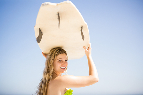 Blonde woman holding surfboard over head at the beach