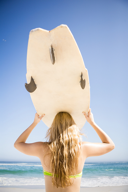 Blonde woman holding surfboard over head at the beach