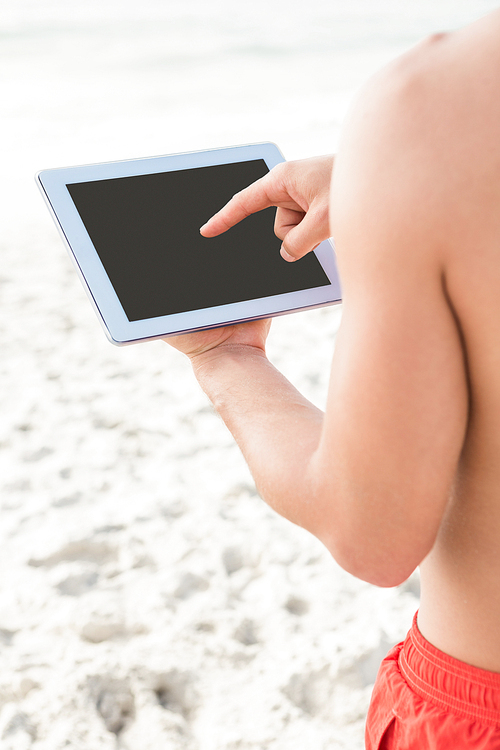 Fit man using tablet on the beach a sunny day