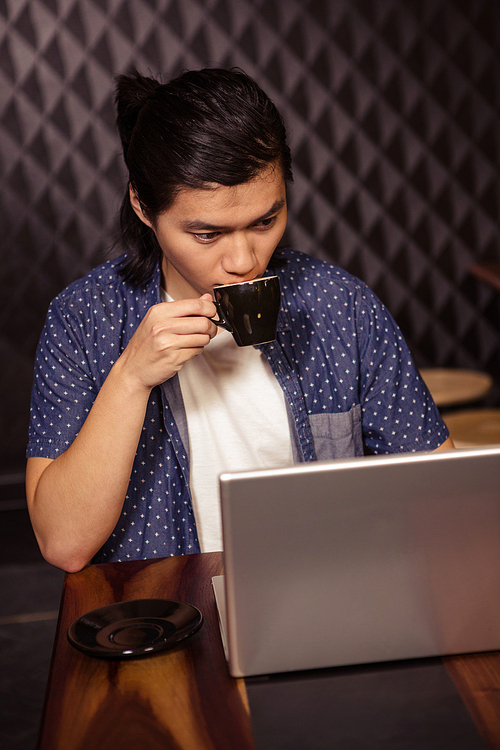 Man using a laptop and drinking coffee in a coffee shop