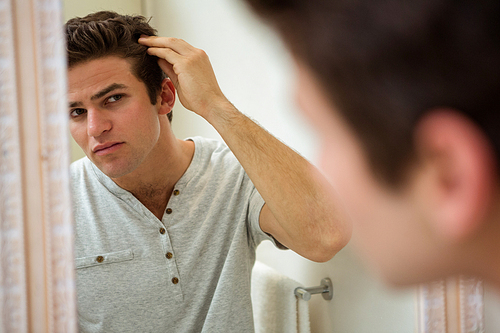 Reflection of young man checking his hair in front of bathroom mirror