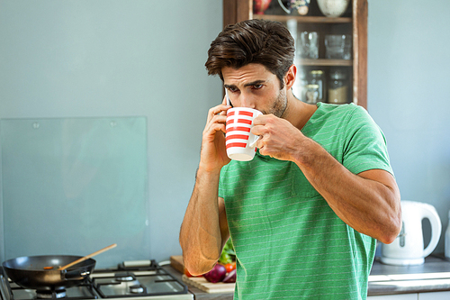 Man having coffee while talking on the phone in kitchen at home