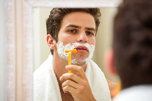 Young man shaving in front of bathroom mirror