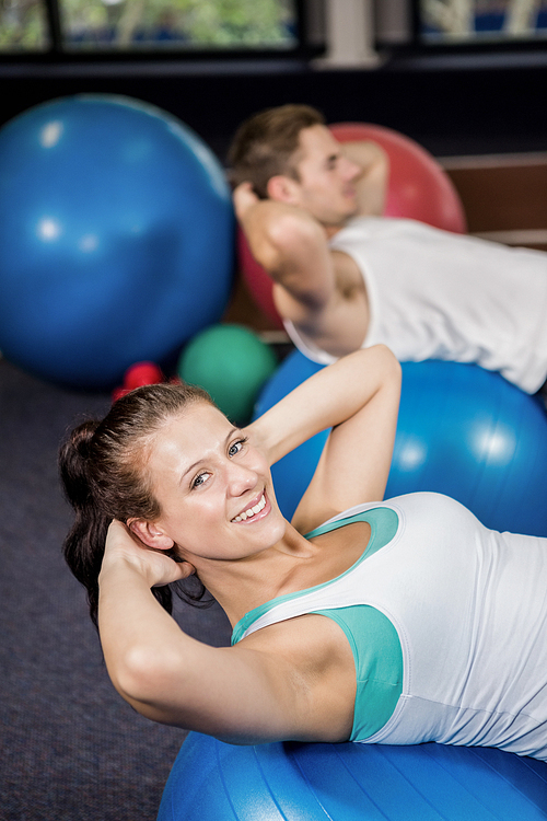Happy woman working out on a fitness ball at gym