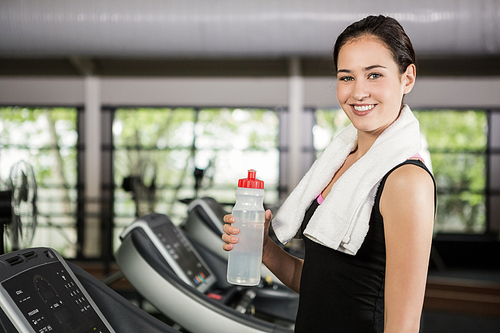 Portrait of happy woman on treadmill holding water bottle at gym