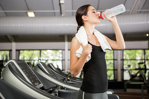 Woman on treadmill drinking water while exercising in gym